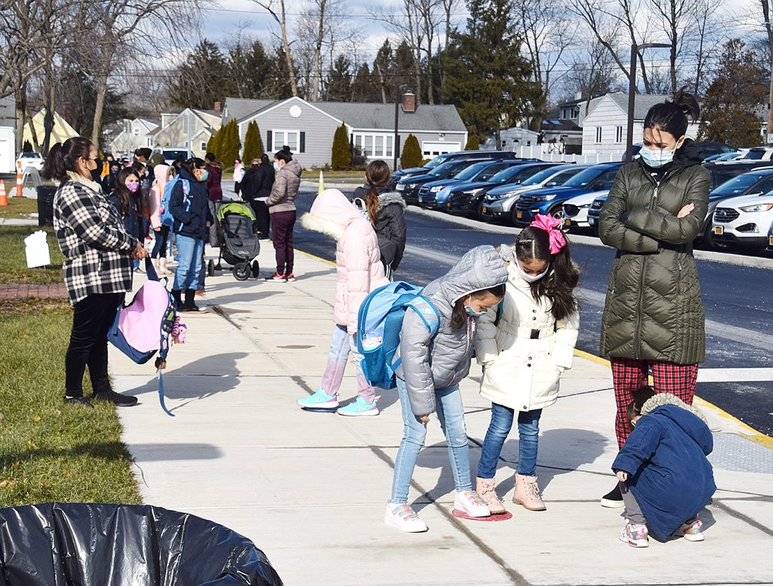 Clusters of King Street Elementary School children and parents use colorful dots on the pavement to stay six feet apart while they wait for the doors to open.