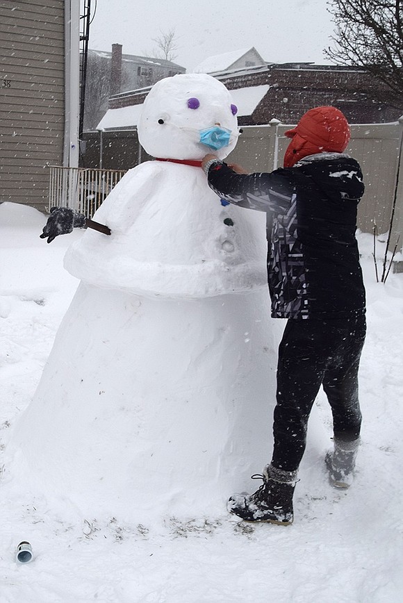 Angelo Farez ties a red ribbon around the neck of the life-size, masked snowman he crafted in front of his house at 38 Madison Ave. All he had left to do was place a hat on the snowman’s head. 