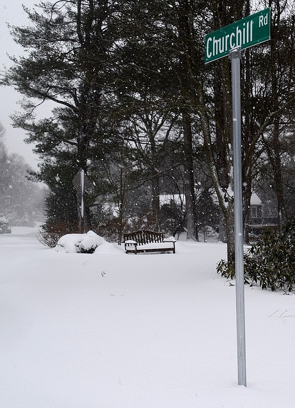 Serene scene of a snow-covered bench on a traffic island on Churchill Road in the falling snow.