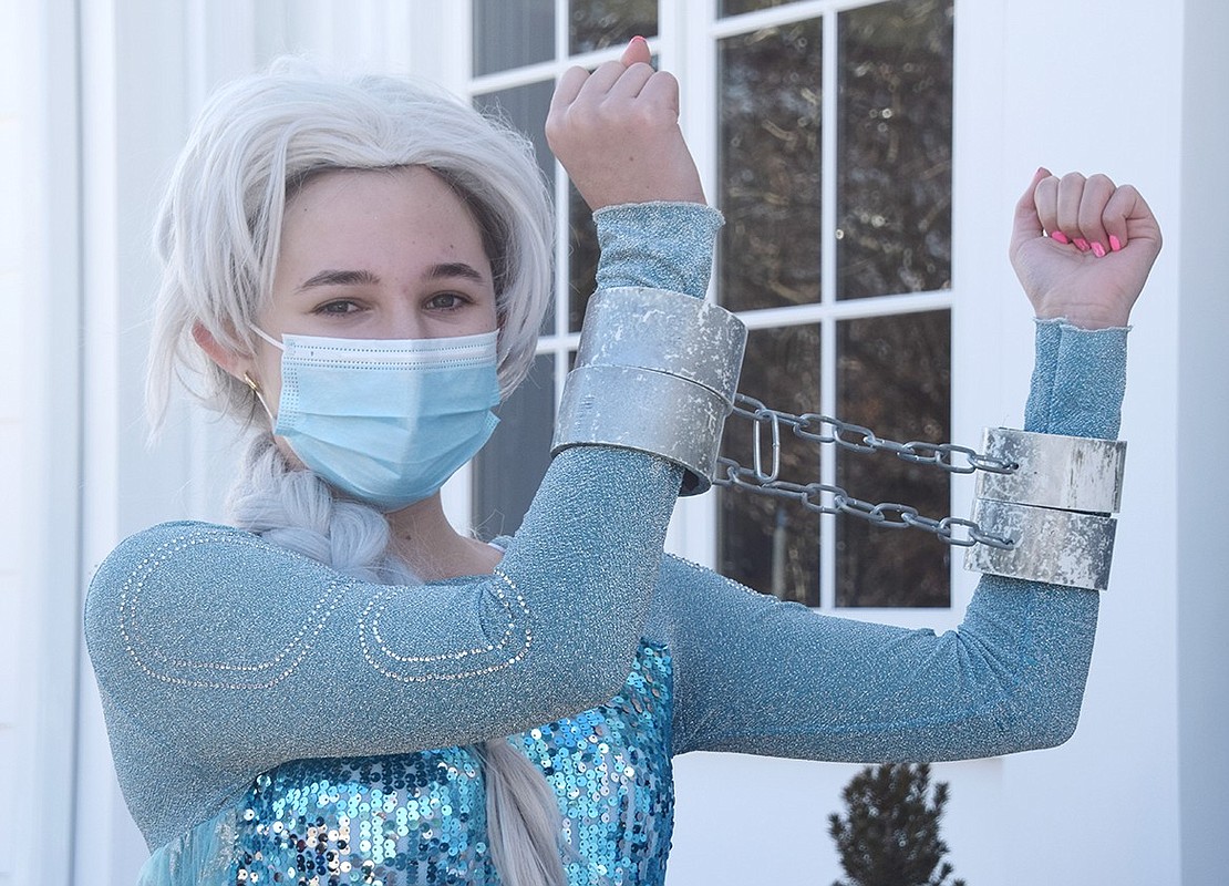 Restrained by enchanted chains that prevent her from using her powers, Elsa (played by Abby Meron) smiles for the camera before pretending to get escorted away.