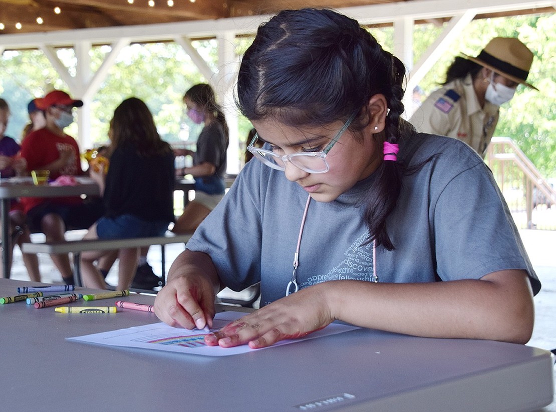 With crayons spread about the picnic table, Ridge Street School third-grader Anvitha Bhatt intently focuses on her colorful American flag drawing.  