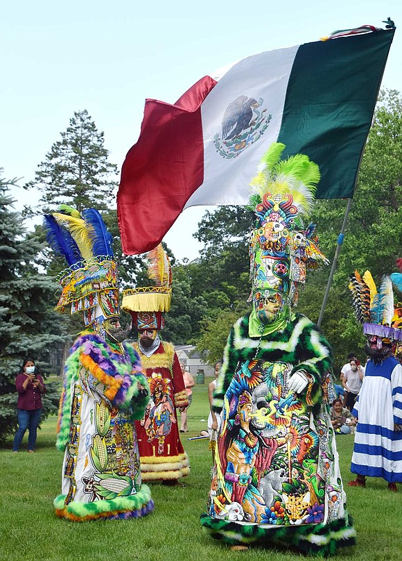 With the Mexican flag waving overhead, a group of performers dressed in gorgeous masks and garb rhythmically dance in front of the showmobile at the park.