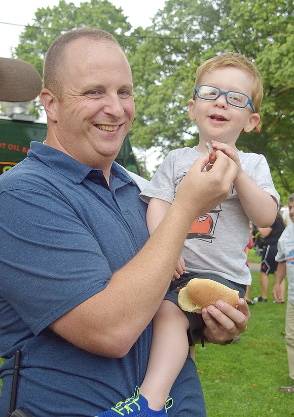 Detective Arthur Dusenbury helps his 2-year-old son A.J. eat a hot dog. No bun is necessary; clearly A.J., full of giggles, is enjoying the meal without one.