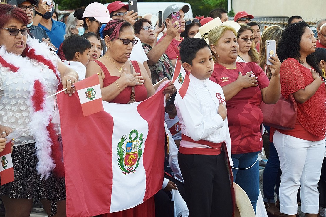 Members of the mostly Peruvian crowd assembled for the celebration put their hands over their hearts and sing the national anthem as Mayor Marino raises the flag.