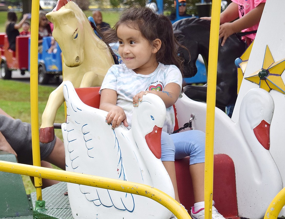 Putnam Drive resident Nina Barrenechea, 4, is thrilled to see her mother as she loops around in her swan seat on the merry-go-round ride.