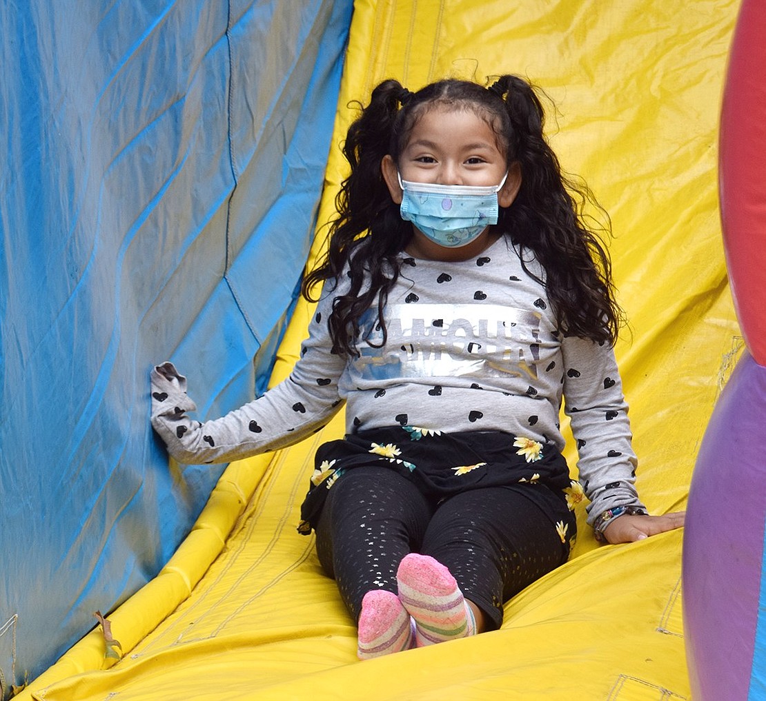The face covering can’t mask the elated grin on Natalie Bracamonte’s face as she bounces down a slide to leave an inflatable bouncy house. The 7-year-old New Rochelle resident is visiting Port Chester Day with her mother, who works at the Port Chester-Rye Brook Public Library.