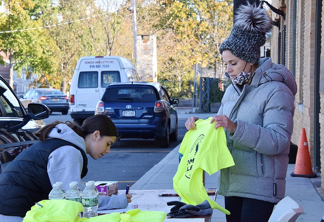 Sofia Larizza, 16, of Hobart Avenue, a sophomore at Port Chester High School, signs up for the Community Cleanup Day in front of the Port Chester train station and Port Chester Beautification Commission member Amanda Barrow hands her a bright yellow T-shirt as a memento of the day.