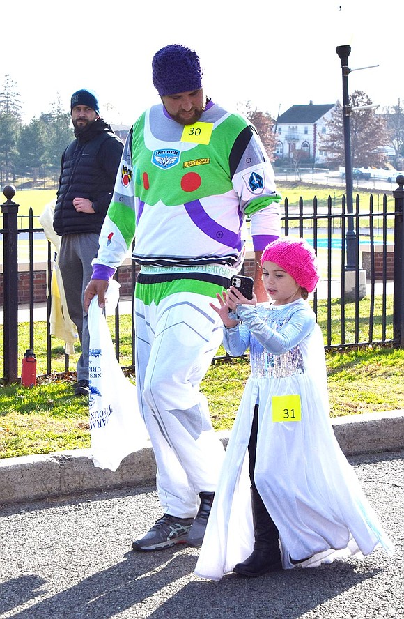 Zach Dore, wearing Buzz Lightyear garb, covers the course with his 5-year-old daughter Annie, dressed as a princess and catching a selfie. They live on Priscilla Lane. 