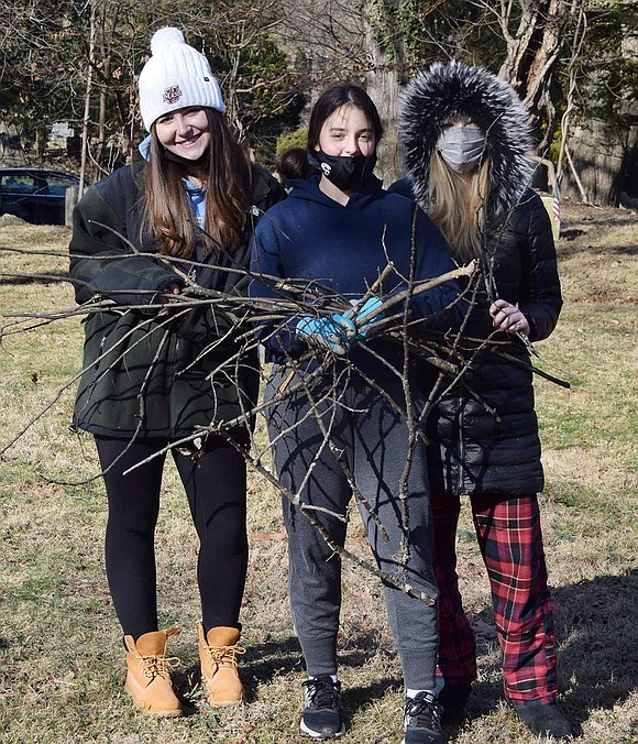 Danielle Orris, Anna Bouadze and Clara Hastings, all seniors at Blind Brook High School, gather sticks they picked up to put into the wheelbarrow for carting away.