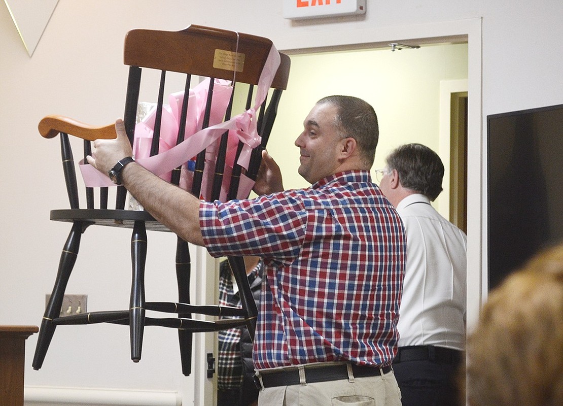 Superintendent of Public Works Michal Nowak lifts up a chair with a nameplate engraved with the outgoing mayor’s name and dates of service, a gift from the village board and administrative staff. 