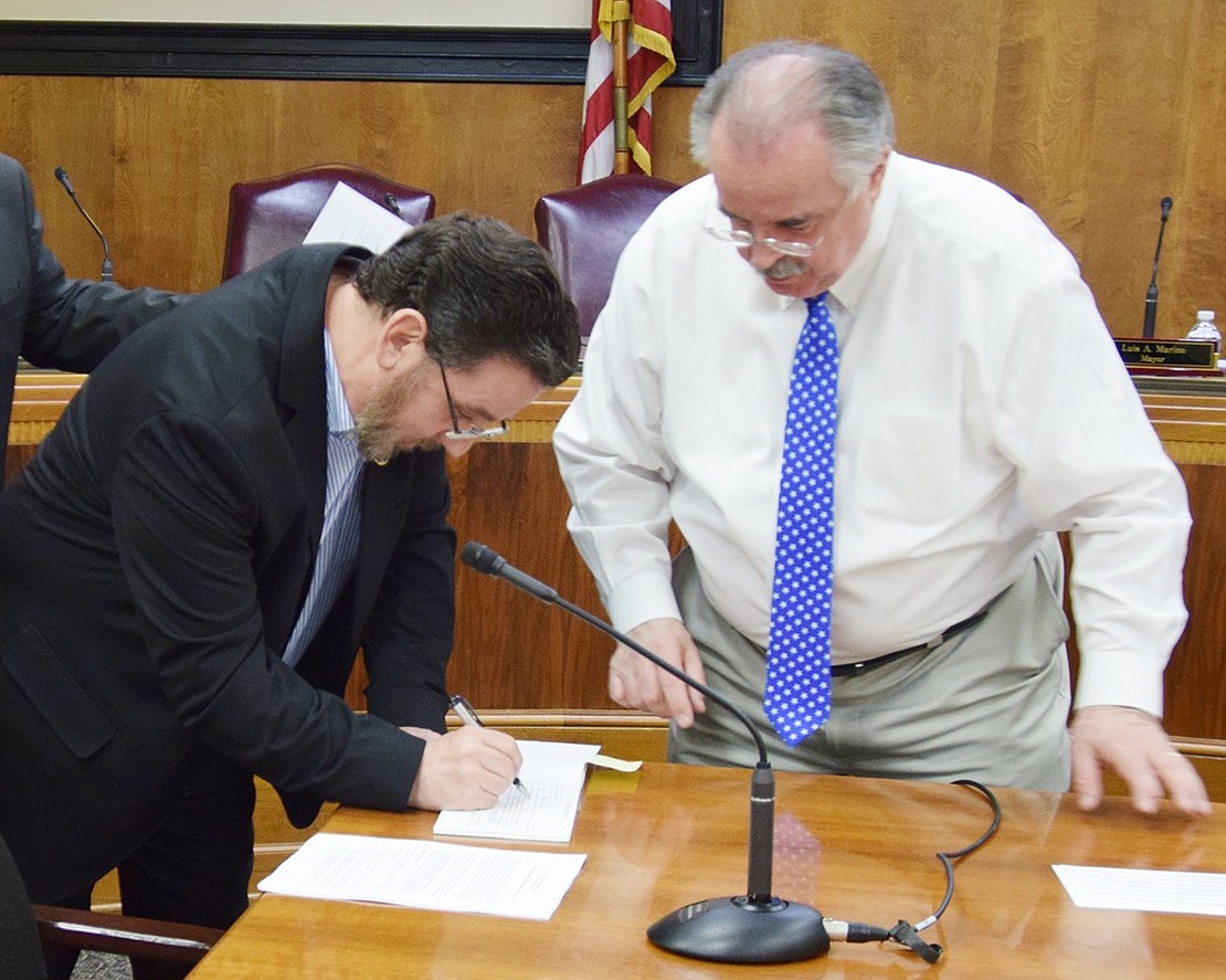 Phil Dorazio signs his oath of office under the watchful eye of Village Clerk Janusz Richards Tuesday night in the Rye Town Courtroom. One year the Democratic trustees failed to sign their oath and special state legislation was required to keep them in office.
