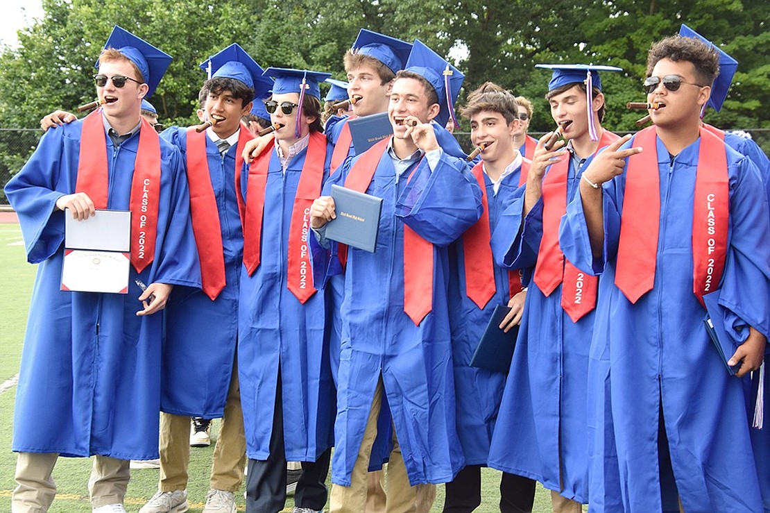 Cigars all around! A group of graduates immediately celebrates their rite of passage into adulthood by partaking in a luxury treat for the mature on the football field.