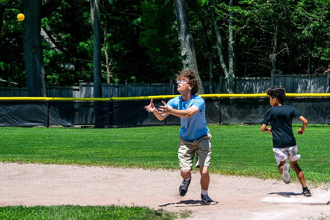 Blind Brook High School rising senior Thomas Wemm stretches out his hands, ready to catch the fly ball that will spell an out against speedy Fabio Garcia, who has already blasted past him to first base.