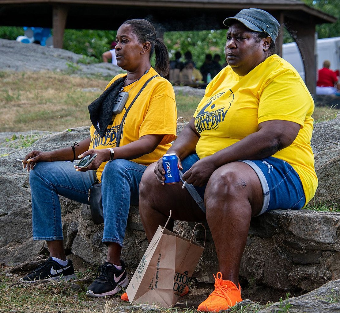 Weber Drive residents Jenita Currie (left) and Evette Vannorden sit on rocks at Columbus Park, chatting as they enjoy food they received at the event and watch the basketball games.