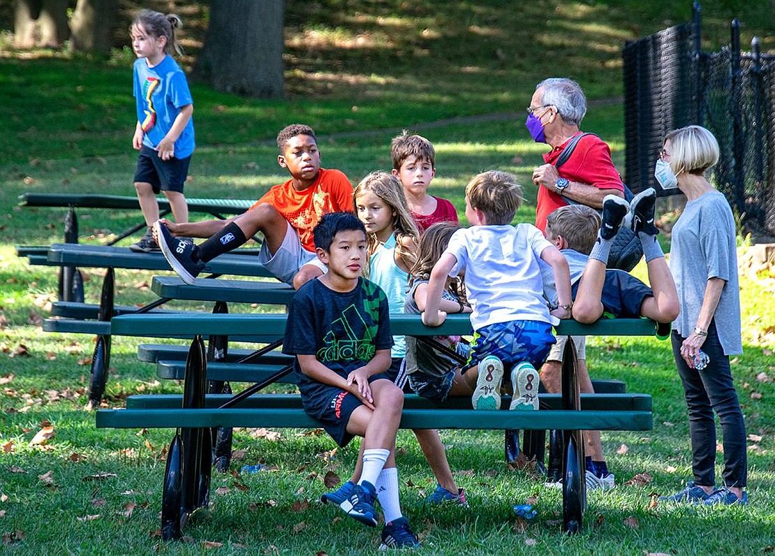 Running around hard at play on a warm summer day can be exhausting. A group of children takes a break on picnic benches that line the fence near the tennis courts.