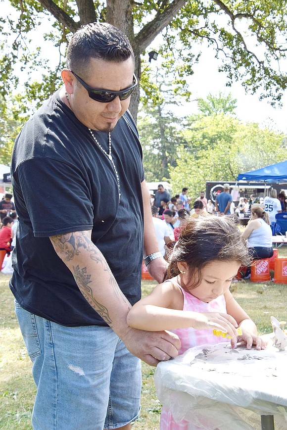 With a cookie cutter in hand, 4-year-old Summer Street resident Isabella Gomez makes her forever mark by carving out shapes at the hands-on Clay Art Center booth with the help of her father William.