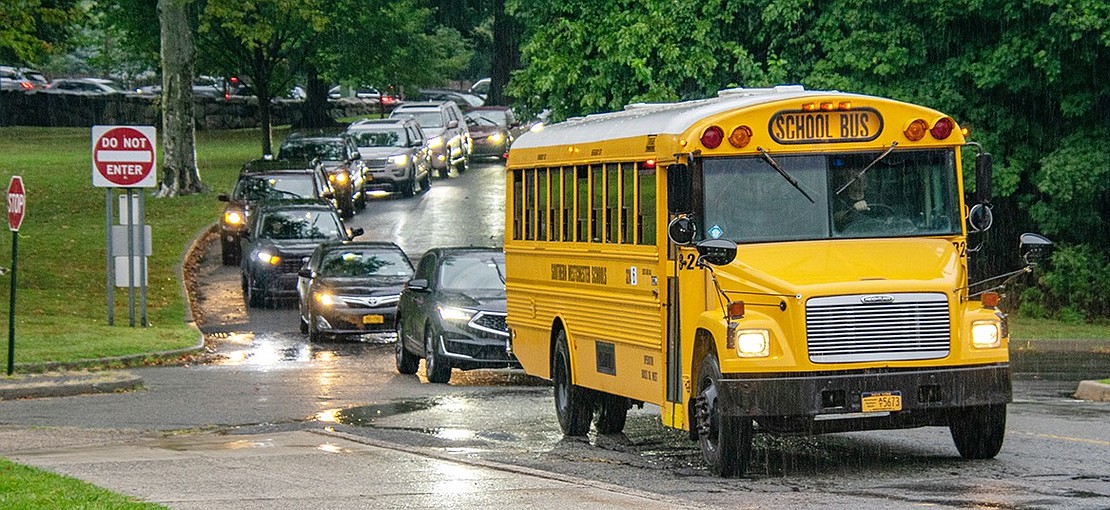 Windshield wipers whip away in the downpour as a school bus leads a line of cars waiting to drop off students at the Blind Brook Middle/High School.