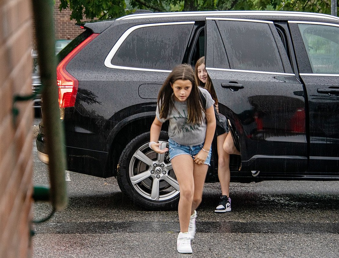 Sixth-graders Tessa Lerch (front) and Charlotte Roseman are ready to run. They bolt from the vehicle dropping them off, hustling inside to get out of the rain and see their peers.