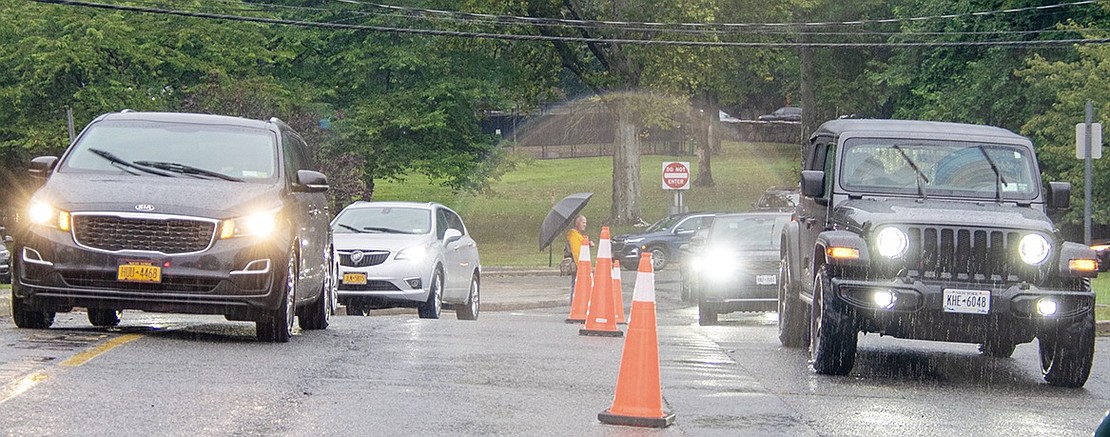 Cars drive up to the front doors of Blind Brook Middle/High School in two lines to drop off students. A crossing guard directs traffic, ensuring safety as students and their parents mosey along in the packed parking lot.