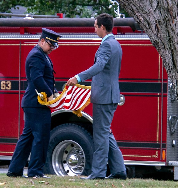 Hugo Vargas (left) and Emmett Dickheiser, the vice president and treasurer of the Putnam Engine & Hose fire company, roll up an American flag used during the ceremony.