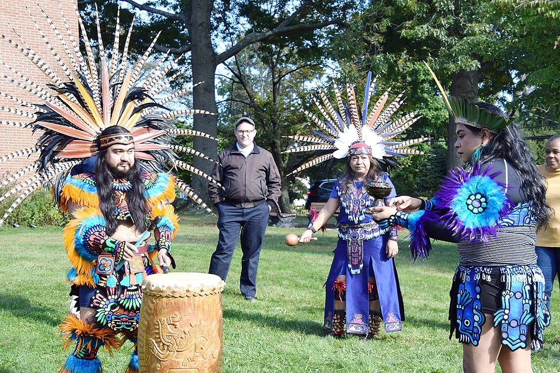 A group of Aztec dancers enthralls a small assemblage of community leaders and other residents (Rabbi Ben Goldberg of Congregation KTI and Port Chester Trustee Joan Grangenois-Thomas pictured here) at the first-ever local gathering to celebrate Indigenous Peoples Day on Saturday, Oct. 8 on the lawn at St. Paul’s Lutheran Church in Rye Brook. On the drum is Armondo Sedano, originally from Morelos, Mexico and now Queens, in the middle is Xochitl Blanca Gomez of Port Chester and at right is lead dancer Dianna Ferrer, originally from Veracruz and now the Bronx. The dancers are carrying on the traditions of their ancestors, the indigenous people of Mexico.