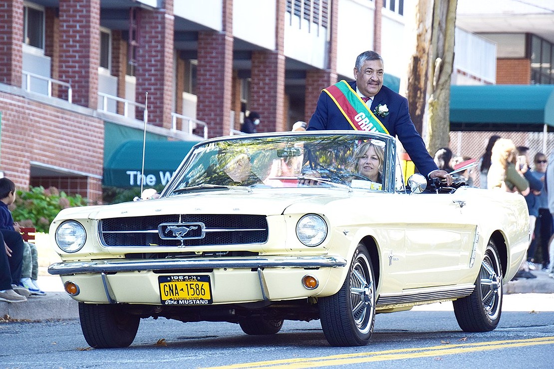 As the parade’s grand marshal, Port Chester Mayor Luis Marino waves an Italian flag and rides down Westchester Avenue in a classic Mustang driven by Betsy Brown Road resident Liz Rotfeld.