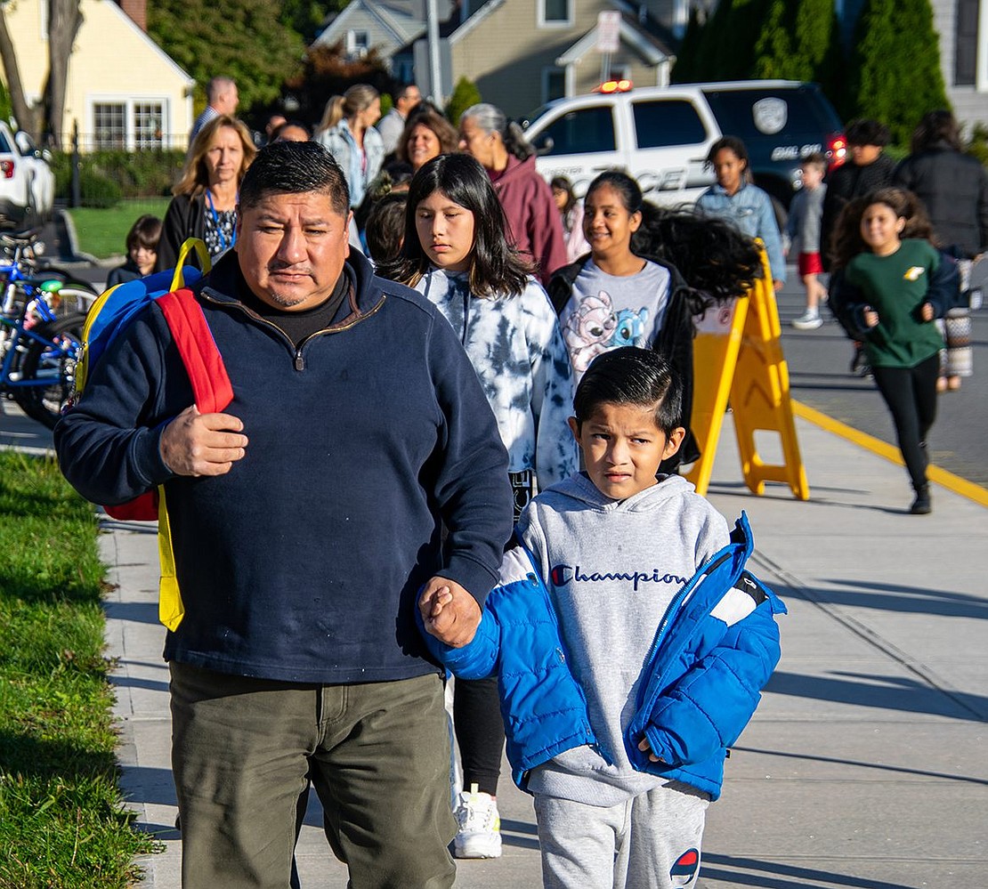 Second-grader David Zhagui holds his father Manuel’s hand as both finish marching around the school’s parking lot with David’s peers.