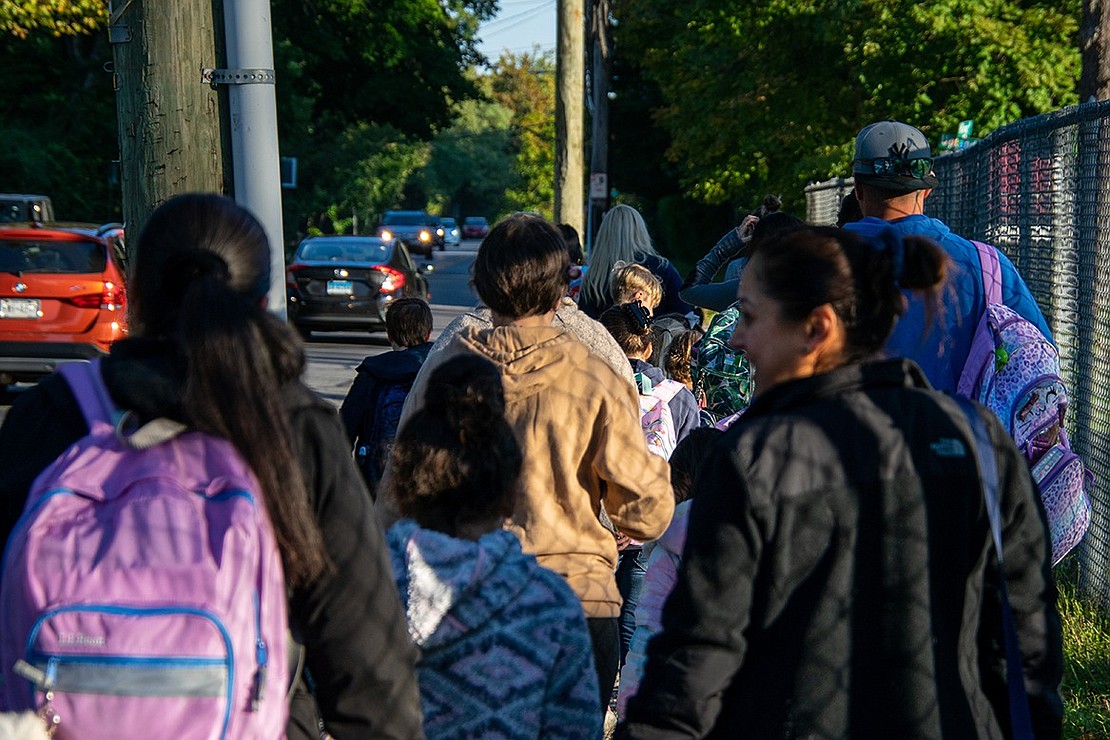 Parents and students walk down King Street to King Street Elementary School for the annual Walk to School Day event. Many of the parents carry their children’s backpacks.