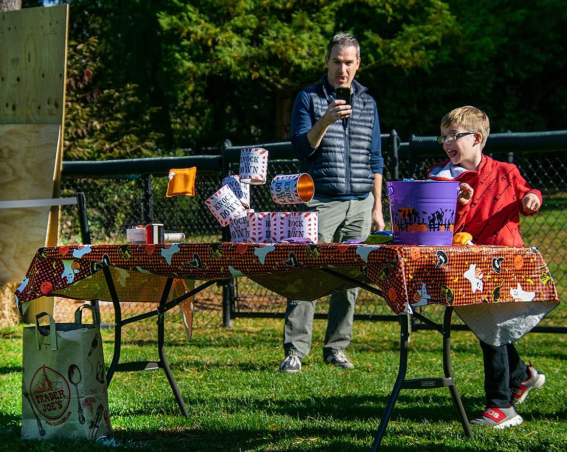 In a show of strength, Cooper Moore whips a bean bag and knocks over the tower of cans in front of him. The Ridge Street Elementary School second-grader’s father Mike records the feat behind him.