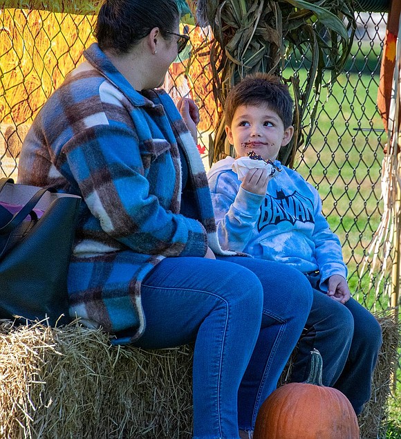 Sitting on a hay bale to take a break, Ridge Street Elementary School kindergartener Jack Bell, 5, devours a doughnut as his mother Kathrine watches him.