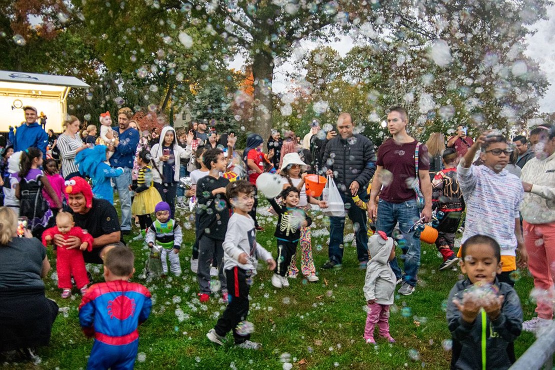 Parents observe their children as a river of bubbles showers them on the park lawn. Many of the little ones are mesmerized by the shimmering orbs.