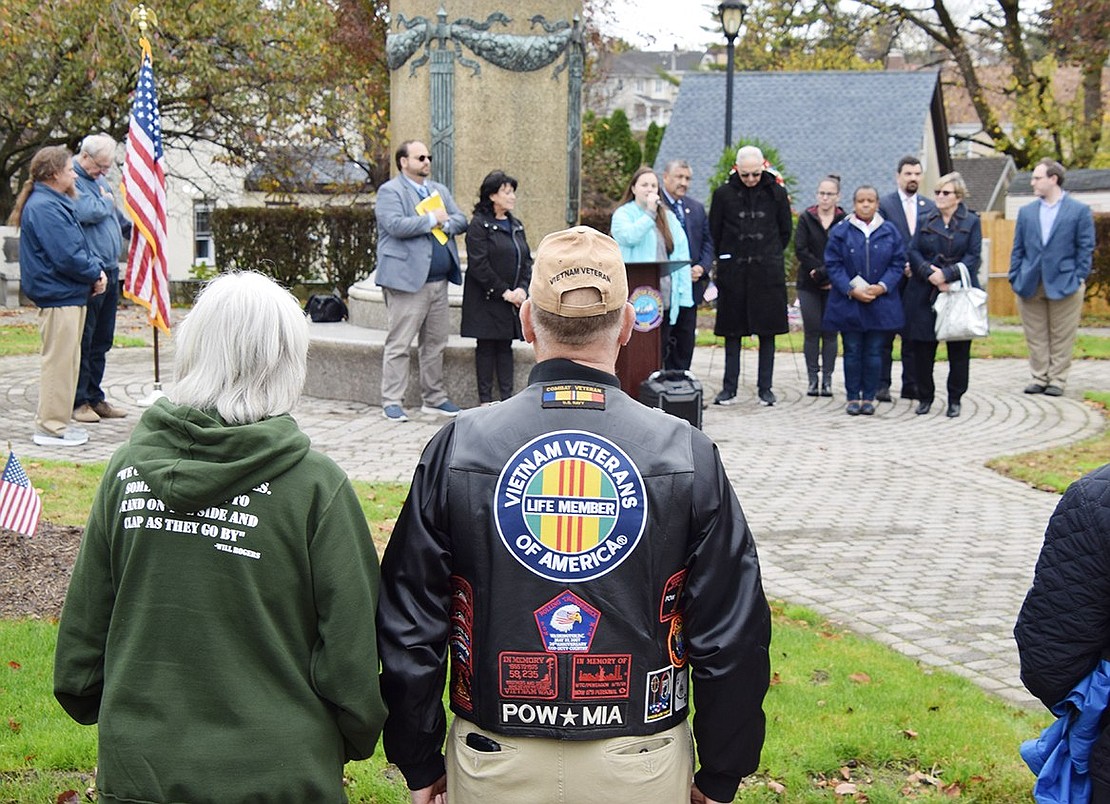 Port Chester residents Mary and Chet Edwards, Chet a Vietnam veteran, stand in the foreground at the Veterans Day ceremony at Veterans’ Memorial Park on Sunday, Nov. 13, while Kim Maguire sings “God Bless America” surrounded by Port Chester, Rye Town and Westchester County officials as well as Rabbi Ben Goldberg of Congregation KTI.