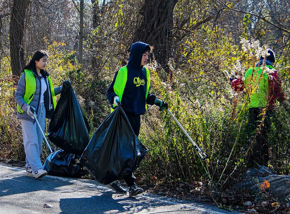 Blind Brook High School juniors Lana Kim (left) and Taka Kimura follow their science teacher Julie Hensley, who searches for garbage in the weeds off Bowman Avenue. The students are members of the school’s Roots and Shoots Club and volunteered on Sunday, Nov. 20 for the organization.