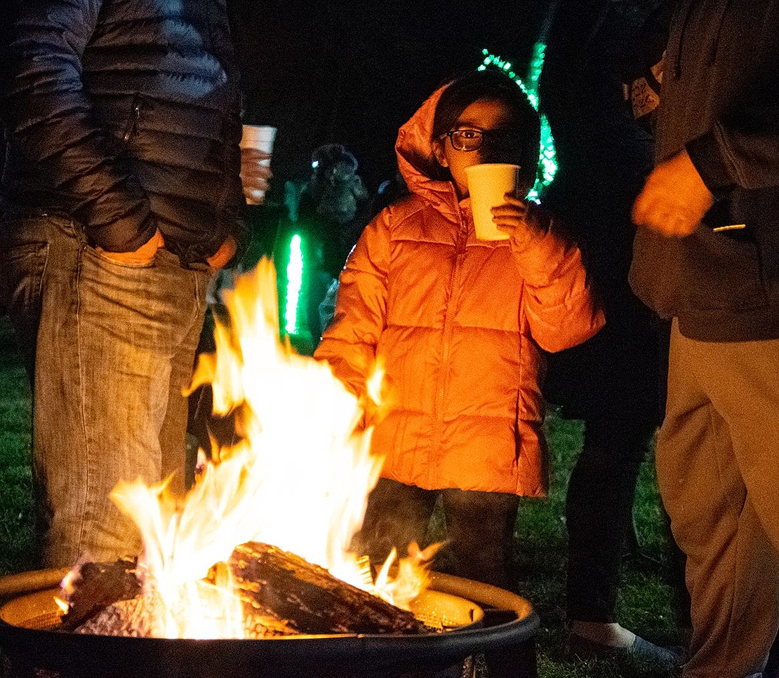 With the temperature dipping to nearly freezing and the wind gusting, Joanna Garcia, 5, warms up with a cup of hot cocoa by a firepit at Crawford Park on Friday, Dec. 9. Behind the Glen Avenue resident, strands of lights line the trees and decorate the lawn for Rye Town’s annual Holiday Lights festival.