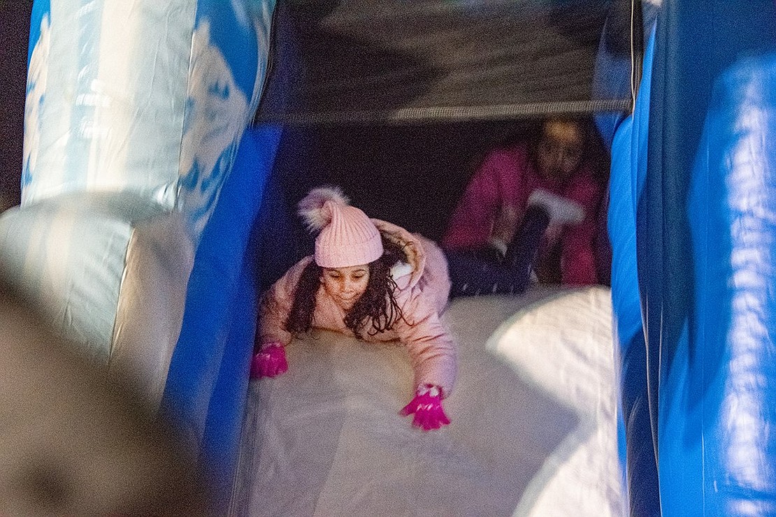 Maya Jimenez, 7, launches herself down a blow-up slide on a bounce house decorated with snowflakes. The Port Chester resident is all smiles as she races the other children navigating the structure.