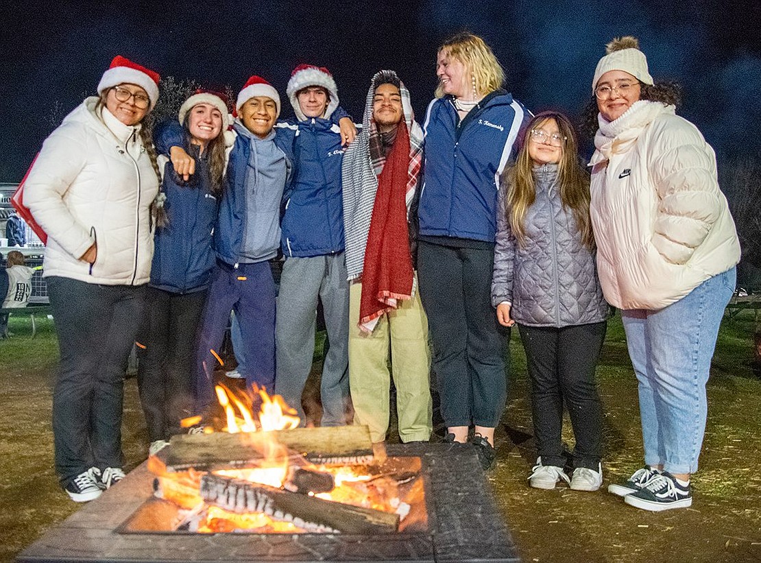 Members of the Port Chester Sound and Port Chester High School band gather around a fire at Crawford Park, having just finished performing in a myriad of musical acts. They spread seasonal cheer with the holiday songs in their repertoire.