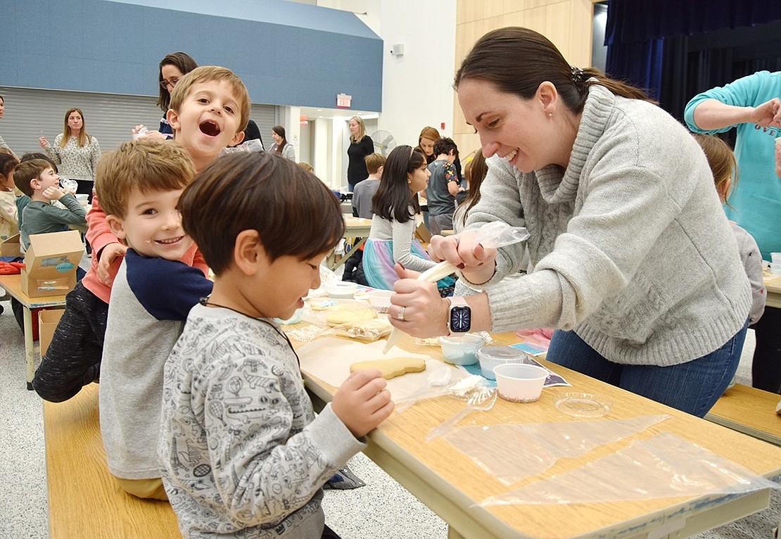 Helping students get a start on their tasty masterpieces, Blind Brook mom Elaine Iarocci wriggles frosting toward the tip of a piping bag while kindergartners Mason Paek (front), Casey Wallace and Sam Sussman eagerly wait. On Monday, Dec. 12, Ridge Street Elementary School kindergarten and first-graders attended a PTA-sponsored cookie decorating fundraiser, while the other grades were invited to do the same the following two nights.