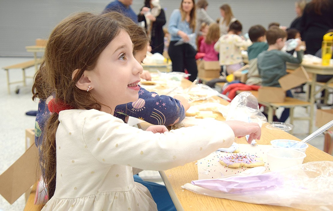 With a yearning grin, first-grader Catherine Iarocci pours several pinches of sprinkles on her purple-frosted cookie, giving it a final razzle-dazzle touch.