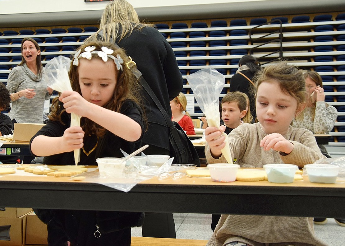 Careful not to break their concentration, kindergartners Riley Cooper (left) and Hannah Stern delicately and artfully adorn their snowman baked goods with frosting.