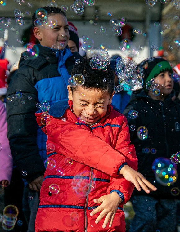 As bubbles tickle his face, Alexander Cuji giggles and squeezes his eyes shut so the suds won’t get in his eyes. The John F. Kennedy Elementary School first-grader waves his arms frantically in self-defense.