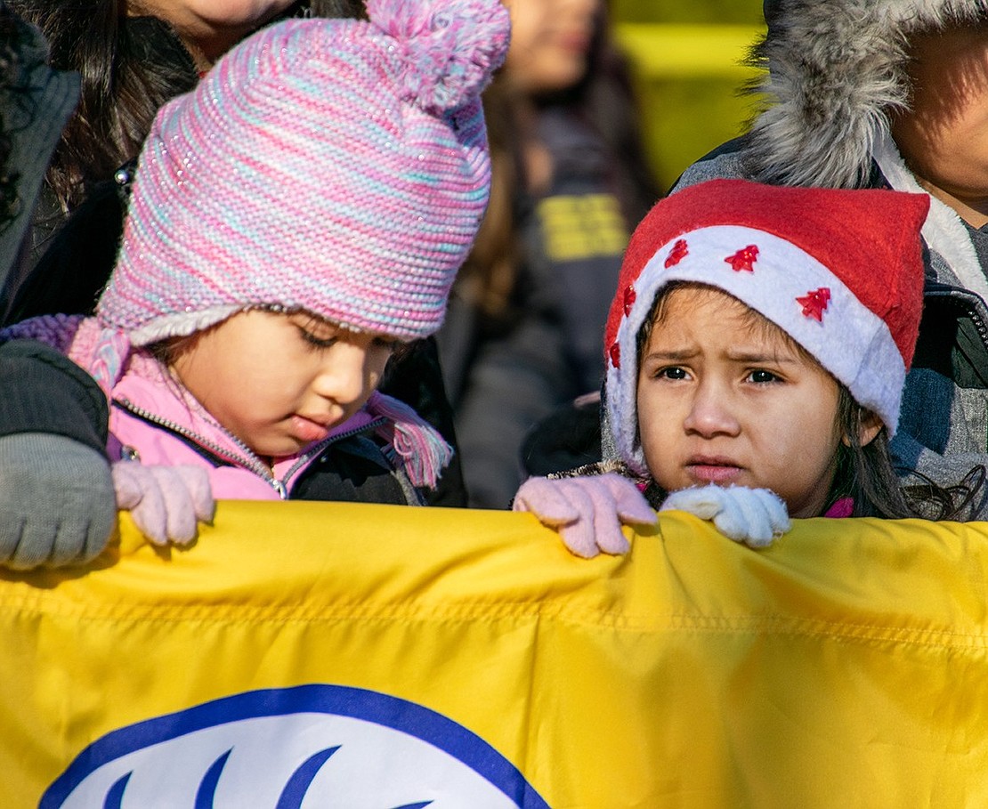 Sara Terrones (left), a John F. Kennedy Elementary School third-grader, makes sure kindergartner Angelica Ramirez doesn’t trip as the two hold up the school’s banner.