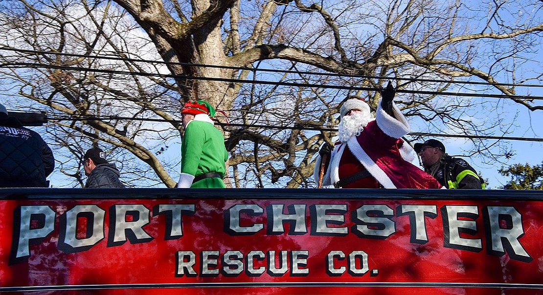 Santa, played by Richard Longo, waves to passersby on Putnam Avenue as he, his elf helper Edward Garrity and several firefighters parade through Port Chester and Rye Brook on a series of engines. Also on top of the truck are firefighter Joe Kempter and Captain Andrew Sposta.