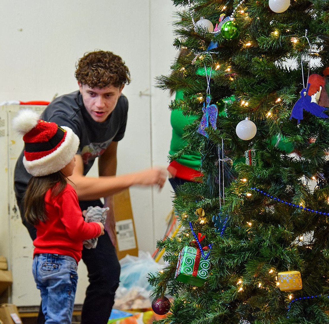 Joshua Negron, a 2022 Port Chester High School graduate, directs 4-year-old Itzayana Hernandez after she sat on Santa’s lap. The young Willett Avenue resident got mixed up trying to leave the stage, overwhelmed by all the gifts the elves handed her.