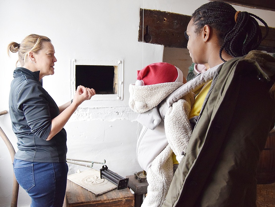 Port Chester Historical Society board member Kikki Short explains to Lupe and Henry Encarnacion and their 6-month-old son Matthew of Austin Place how the brick oven in the wall next to a fireplace at the Bush Lyon Homestead worked in days gone by.