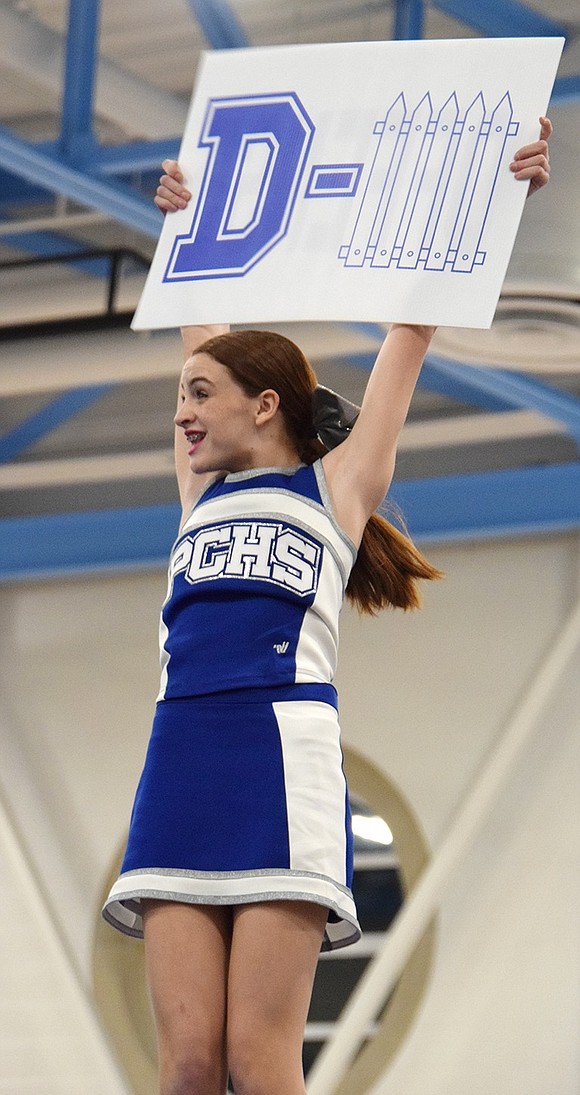 Waving a clever sign while suspended in the air, Port Chester High School freshman Charlotte Burke, a varsity flyer, shows the crowd how to cheer for the defense.