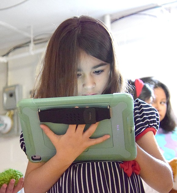 The glow of an iPad illuminates Park Avenue School first-grader Dalia Delakas’s face as her engrossed eyes fixate on robot coding during the Techno Teams, a Girl Scout robotics club, demonstration.