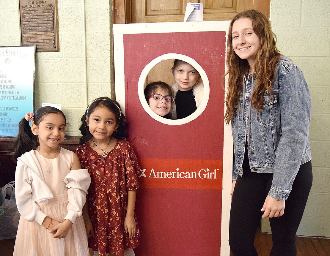 Volunteering at the party, Port Chester High School senior Jenna Provenzano poses for a photo with Park Avenue School first-graders Michaela Lopez (left), Hope Camacho, Piper Webber and Gabriella Giordano around the American Girl Doll box. As a senior, Provenzano is one of the Scouts who will benefit from a scholarship financed by the fundraiser.