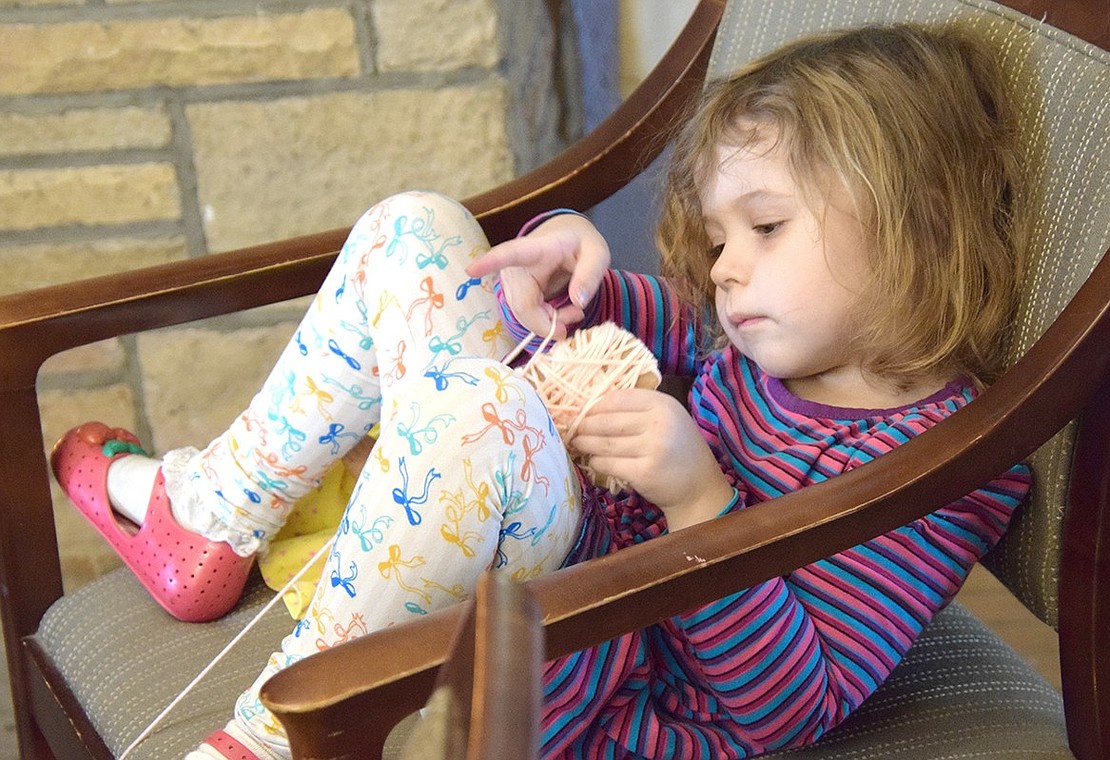 Leona Salzman-Deis, a 4-year-old Port Chester Schools Universal Pre-K program student, cozies up in a chair by the fireplace to distract herself with a yarn activity while the other tea party attendees play bingo.